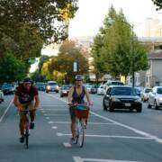 Happy bike riders making their way down an extra wide bike lane on a verdant street.