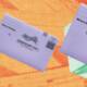 Alt text: Three vote-by-mail return envelopes are arranged diagonally across a bright orange and yellow halftone background. Two smaller envelopes on the left appear blurred, while a larger, sharper envelope on the right rests over green ballot materials and is labeled “Return Envelope,” “Official Election Mail,” and “Business Reply Mail.”