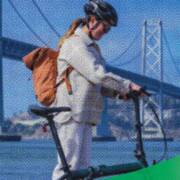 A cyclist with a backpack walks alongside an e-bike on San Francisco’s waterfront, with the Bay Bridge in the background, overlaid with blue halftone texture and green graphic waves.