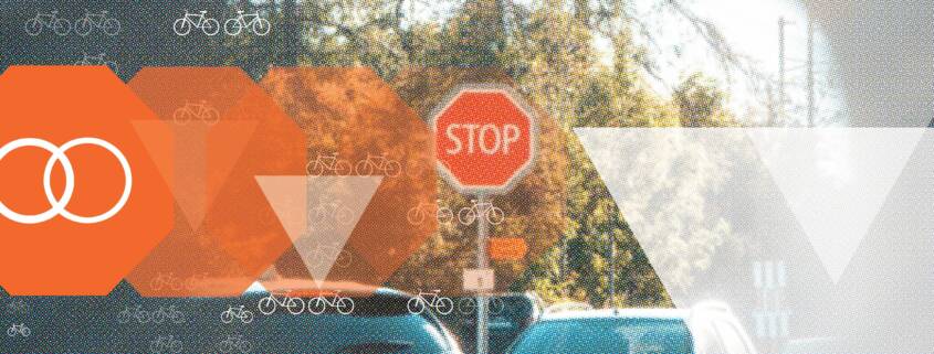 Orange stop signs give way to white yield triangles over a street scene dotted with bicycle icons, illustrating the Bicycle Safety Stop. A sign of progress.